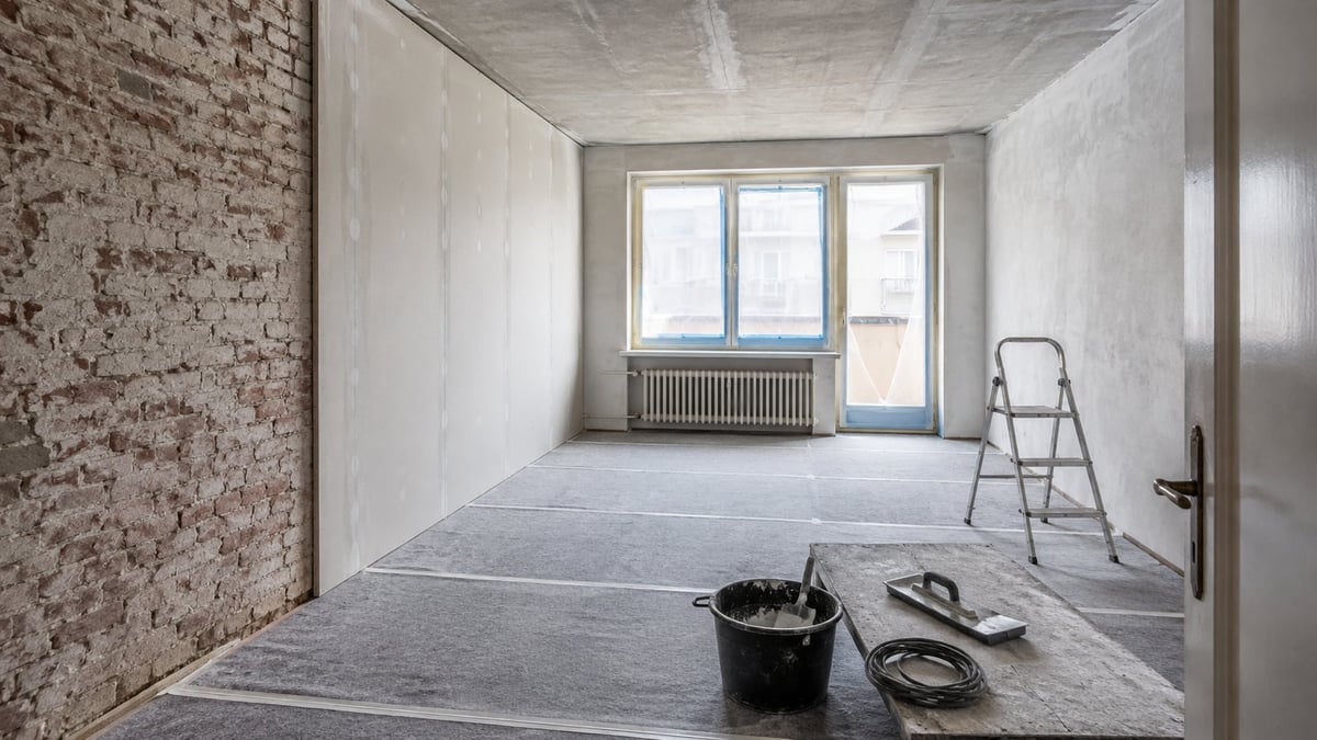 Leerer Raum während einer Renovation mit freigelegtem Mauerwerk, geschütztem Boden, Leiter und Baumaterial
